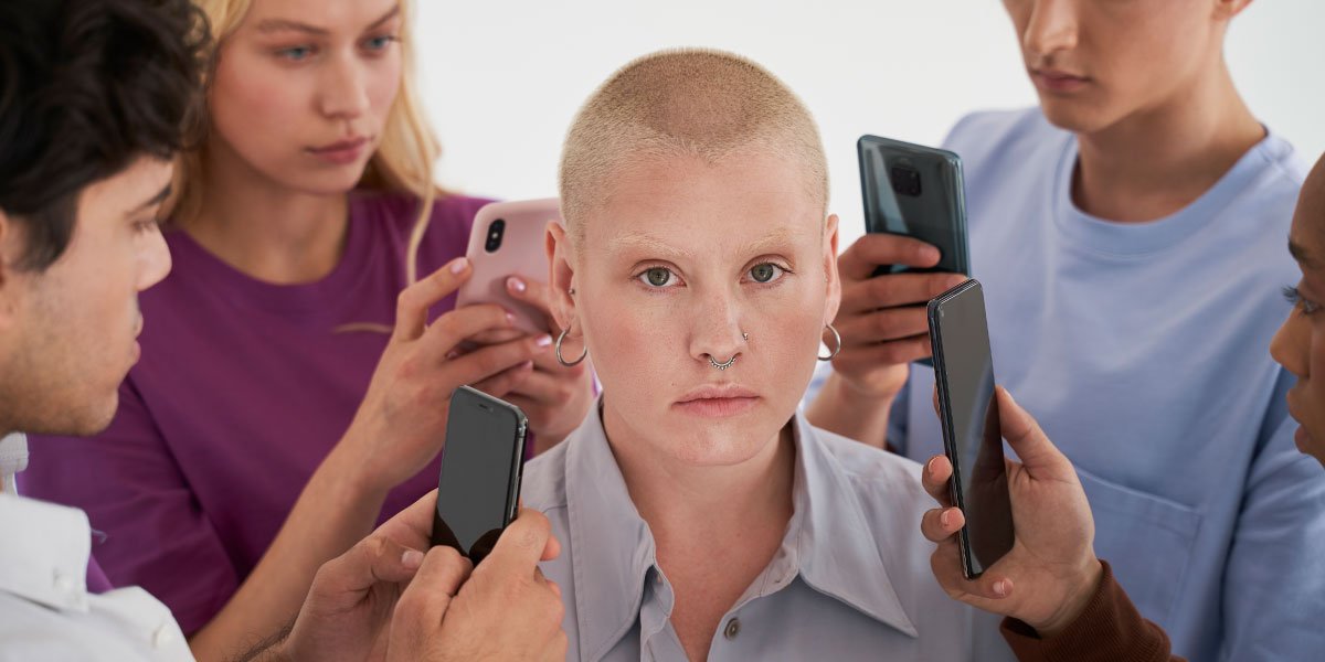 Ein Mädchen im Teenageralter, umgeben von anderen Teenagern, die ihre Smartphones benutzen und sich ängstlich und isoliert fühlen