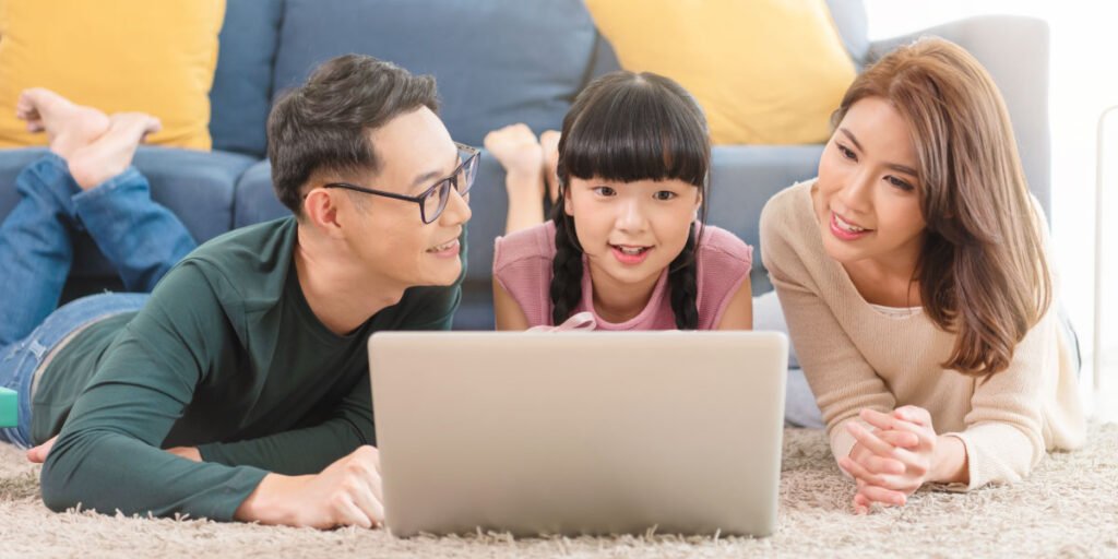 Image of an Asian father, daughter, and mother lying in front of a laptop