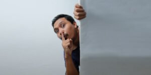 A man making a silence gesture taking a sneak peek from behind a wall