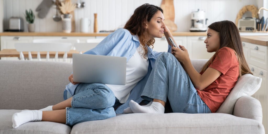 Eltern halten Laptop, während sie versuchen, das Telefon ihres Kindes auf einem Sofa zu sehen