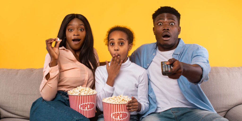 An African family of three (mother, father, & daughter) eating popcorn and watching a program on GOtv, shocked by the inappropriate content