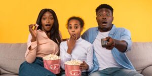 An African family of three (mother, father, & daughter) eating popcorn and watching a program on GOtv, shocked by the inappropriate content