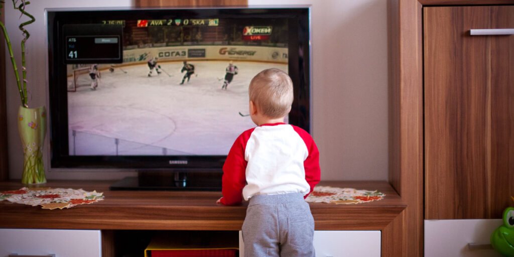 Baby standing in front of a TV showing sports