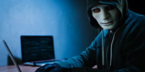 Image of a masked man looking at the camera while typing on a laptop