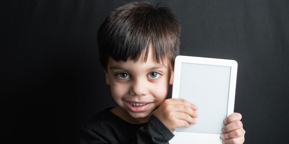 A little boy smiles while holding an e-reader