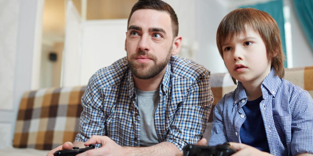 Father and son playing Xbox with popcorn in front of them