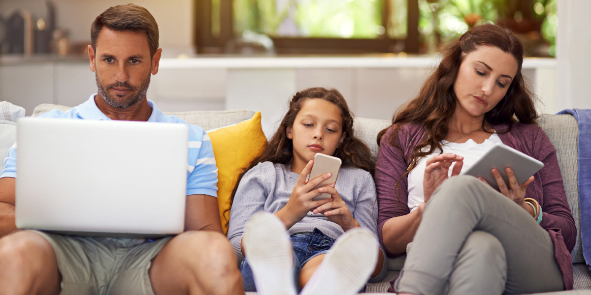A father, mother, and daughter sitting on a couch, consumed by their digital devices