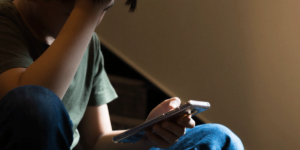 Little boy using a phone while sitting on the stairs with his hand holding his head