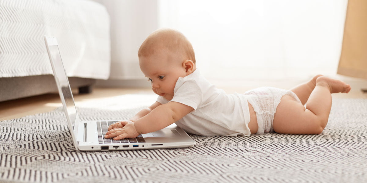 Ein Kleinkind legt sich hinter einen Laptop