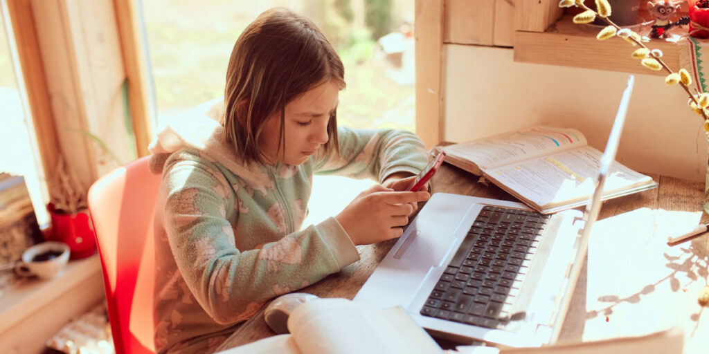 Schoolgirl typing on her phone with books around her