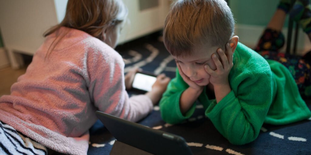 Two children lying on the floor using electronic devices