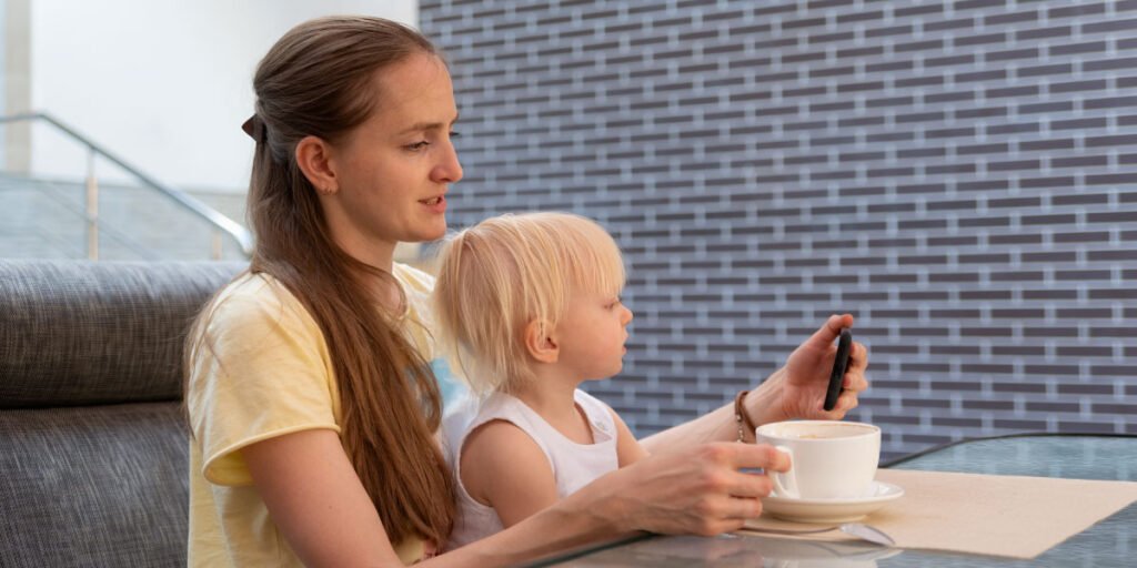 Mutter blickt in einem Café auf ihr Telefon, während ihr Baby auf dem Schoß sitzt