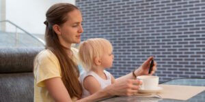 Mother looking at her phone in a café with her baby sitting on her lap