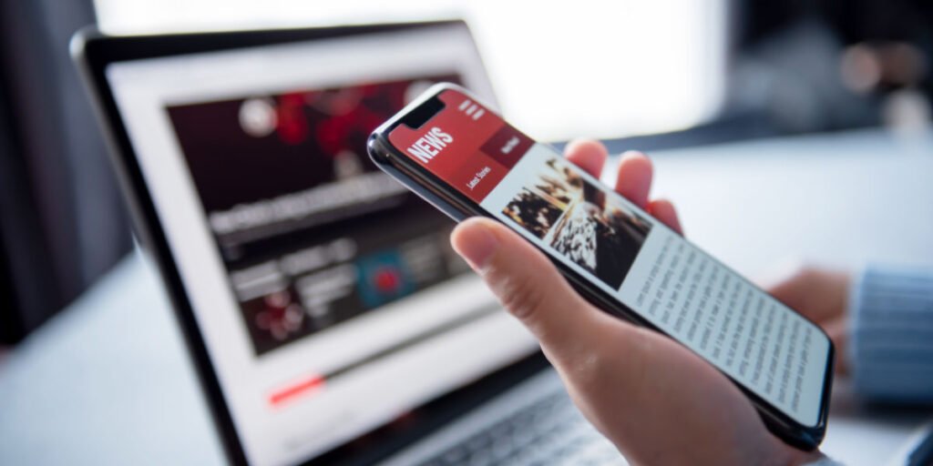 Person reading News on smart-phone and laptop