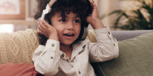 Little boy smiling and wearing headphones with his hands on his headphone.