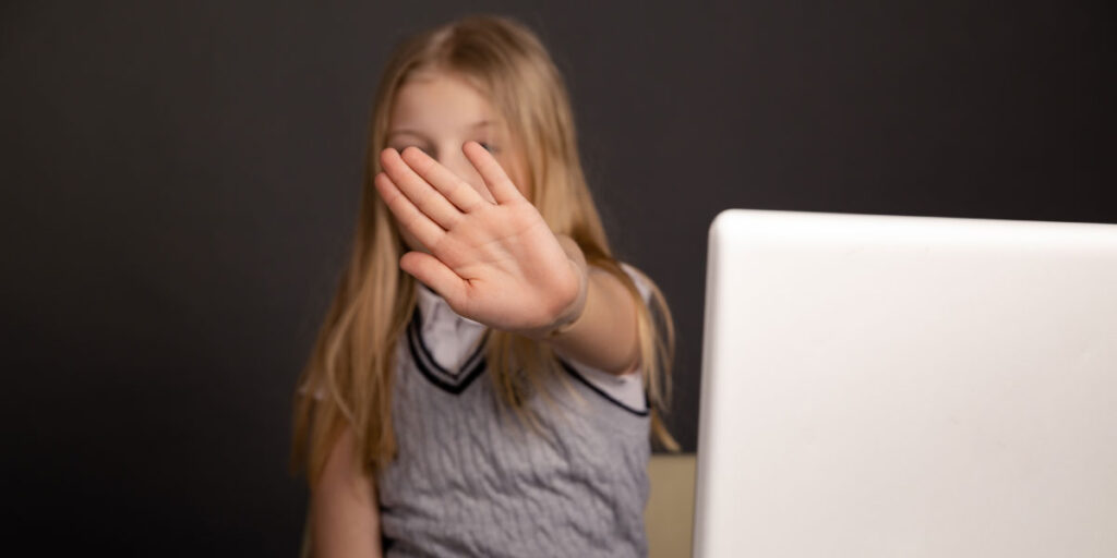 Angry kid showing stop sign isolated in front of a computer