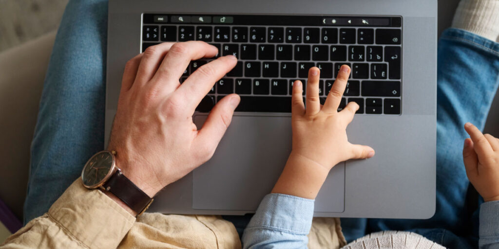 Parent’s and baby’s hand on laptop.