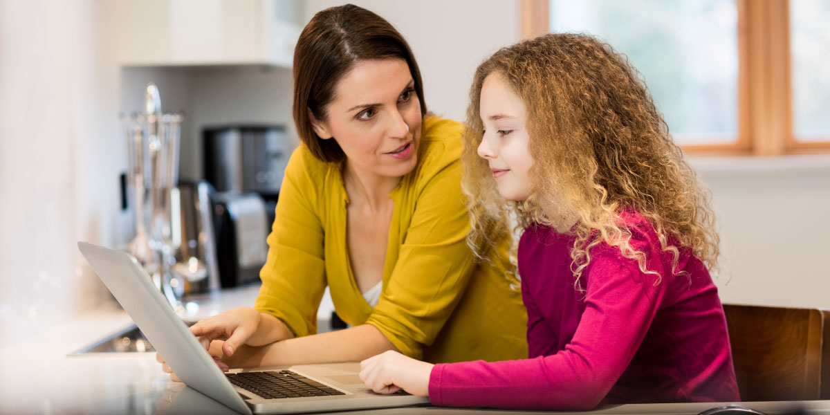 Mother and daughter use laptop in kitchen