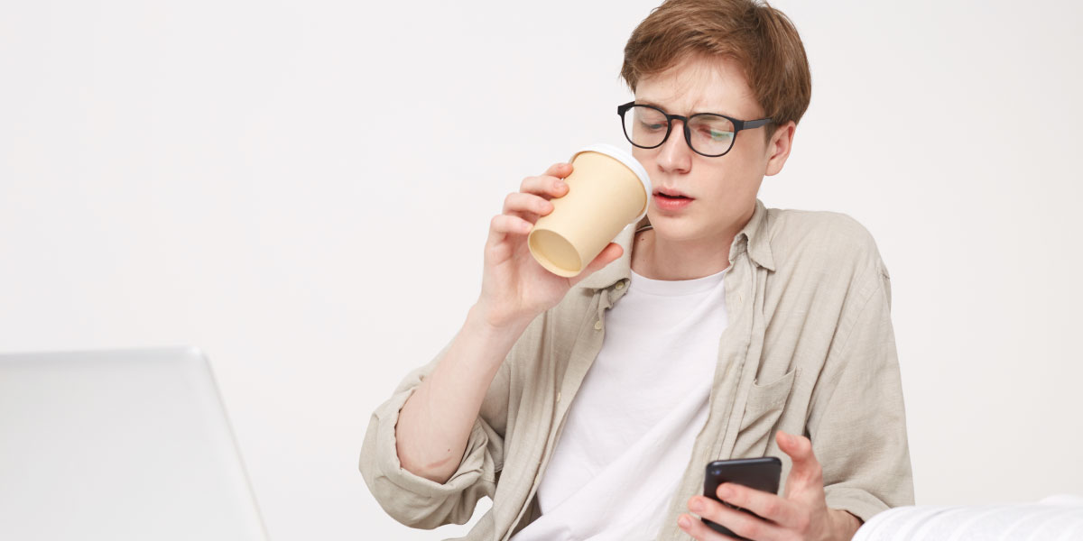 Teenage boy drinking coffee looking at phone with books around