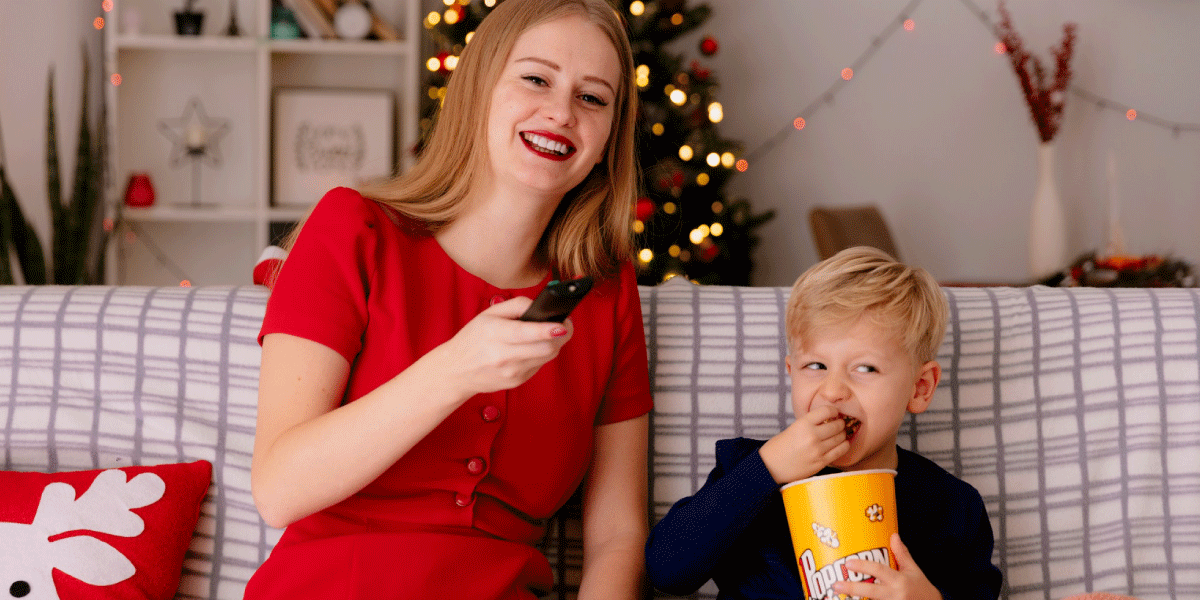 child eating popcorn and watching television with his parent