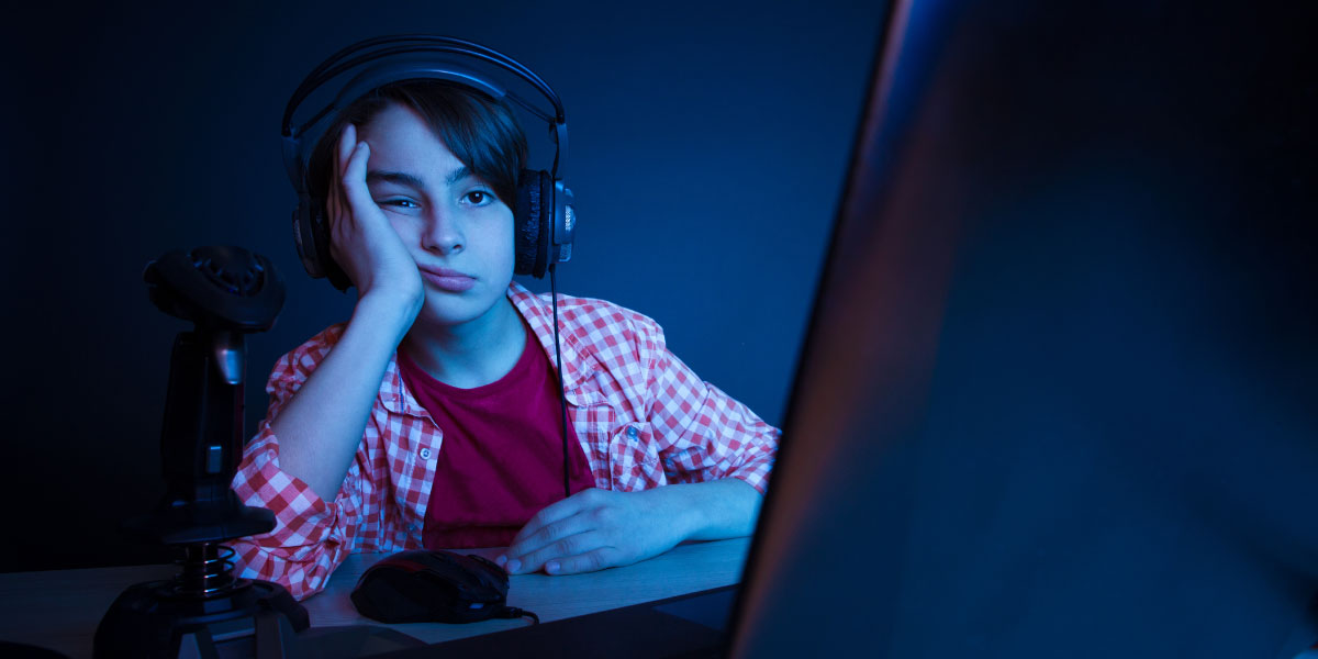 Boy wearing headphones and sitting in the dark looking at a laptop screen