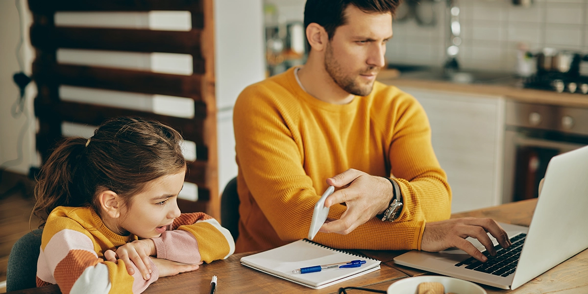 Father working on a laptop while showing a video to his daughter