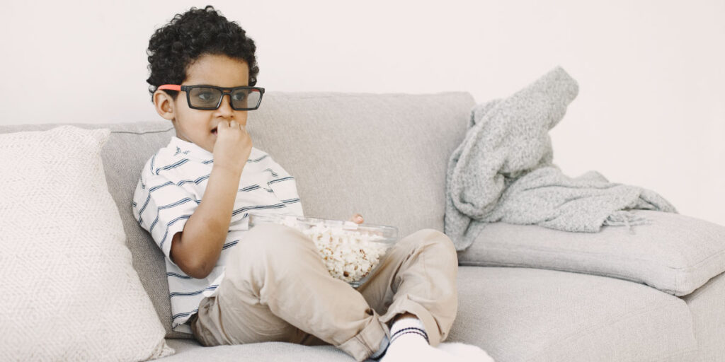 Boy with glasses eating popcorn and watching a movie