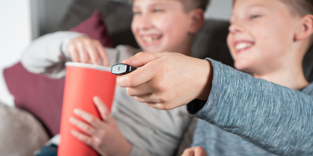 two happy boys eating popcorn and holding the remote