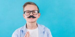 boy wearing black eyeglasses holding black mustache prop