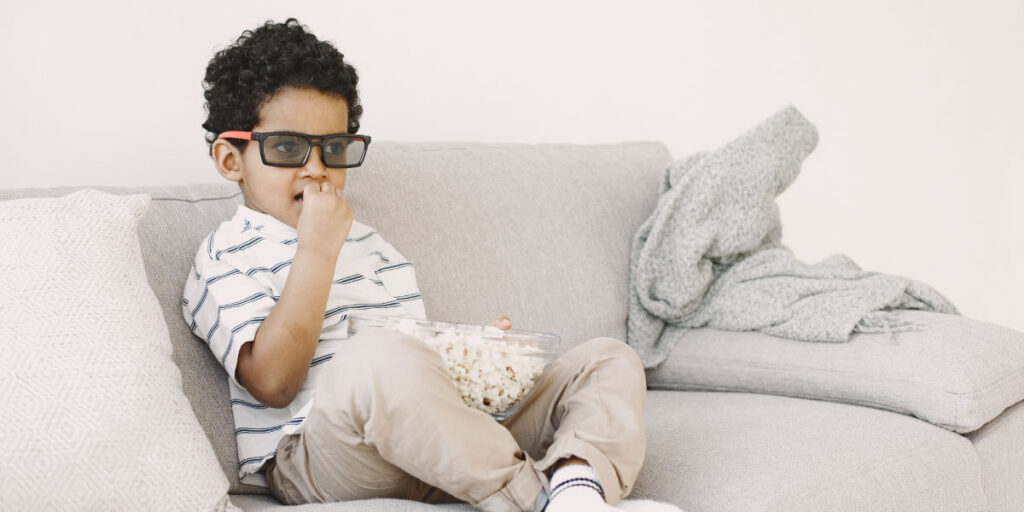 صبي يجلس على الأريكة مع وعاء من الفشار في حضنه