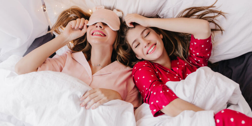 Zwei Mädchen tragen ihren Pyjama und liegen auf dem Bett unter der Decke