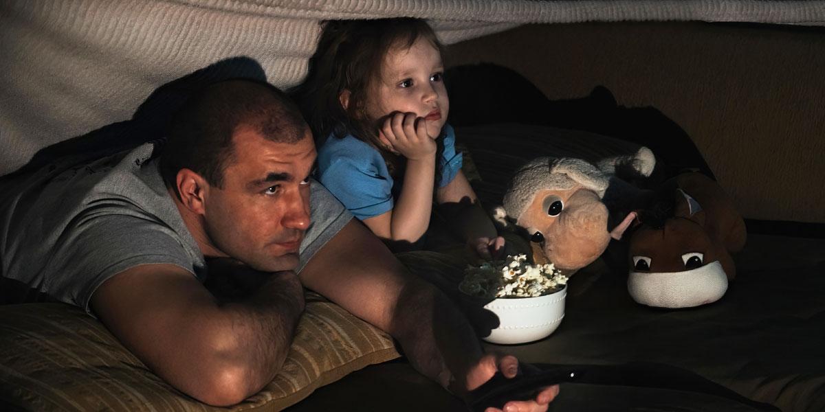 Father and child watching a movie under a blanket