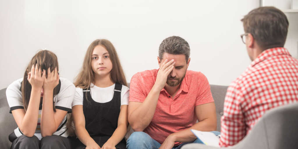 Parents holding their heads in a therapist’s office while a teenager looks into the camera