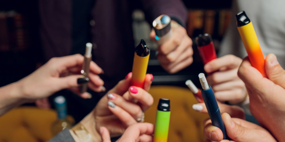 7 hands holding different colorful vaping sticks