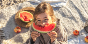girl sitting at the beach with a watermelon slice in front of her mouth