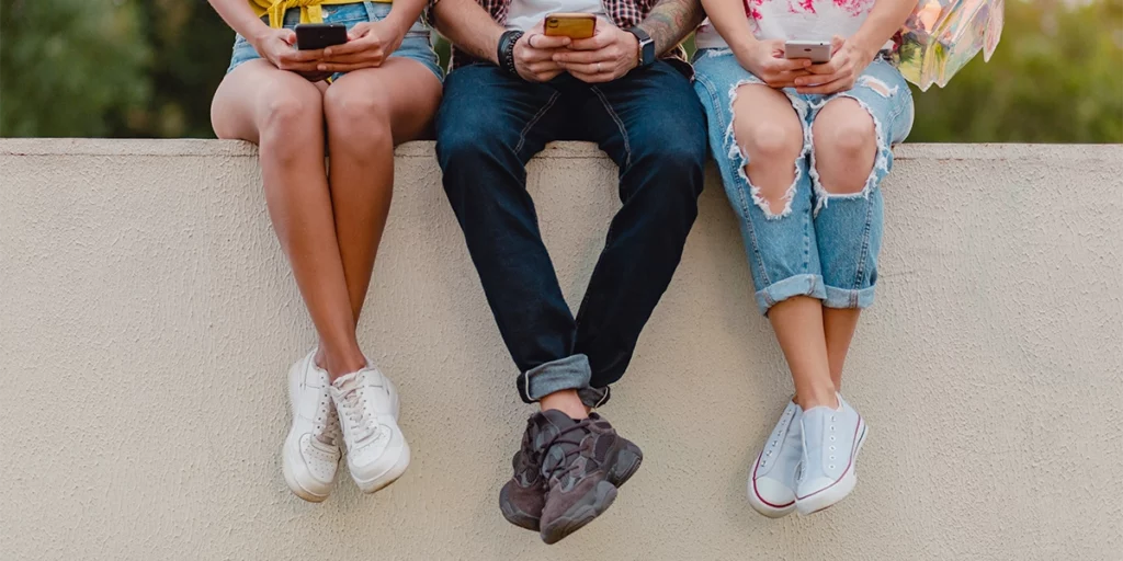 three students sitting on a wall and using their phones