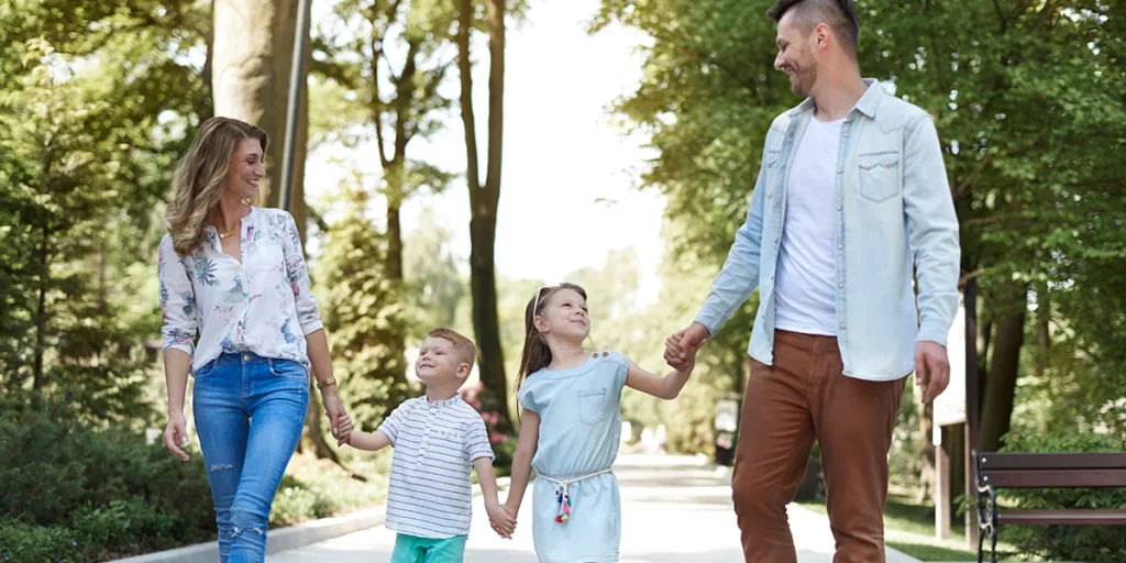 Father and mother holding their daughter and son’s hands walking in the park