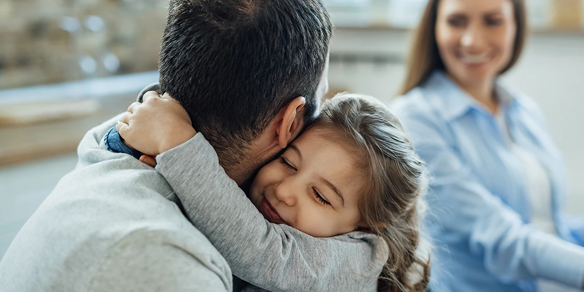 liebevolles kleines Mädchen mit geschlossenen Augen, das ihren Vater zu Hause umarmt