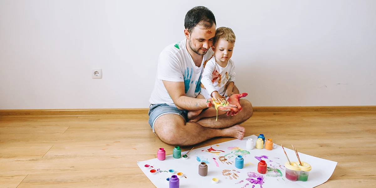 father fingerpainting with his son on the floor