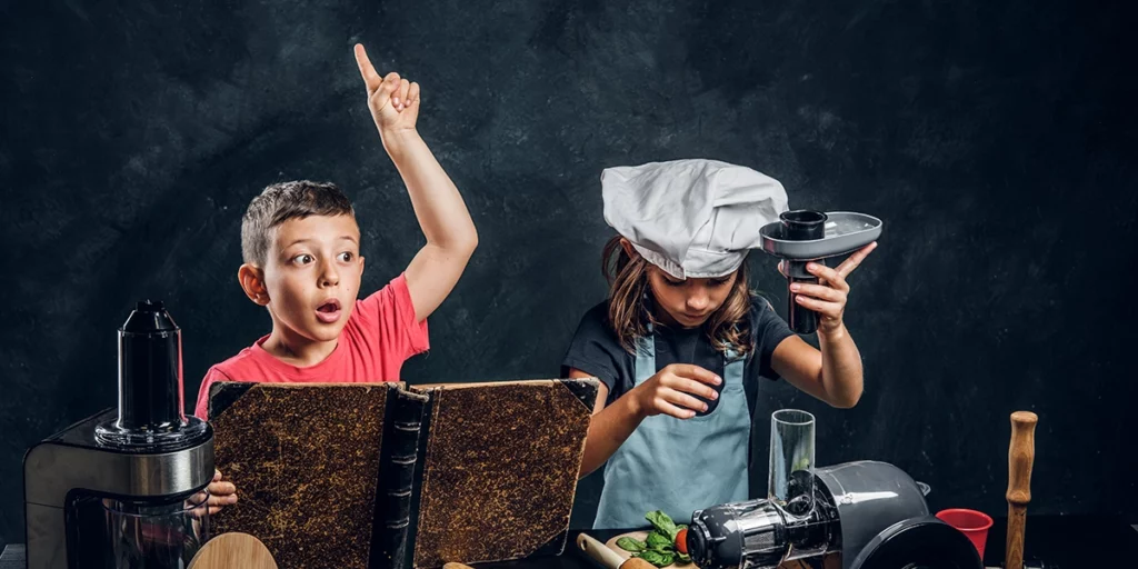 Boy and girl cooking in a kitchen with the boy holding his hand up trying to ask a question while holding a cookbook