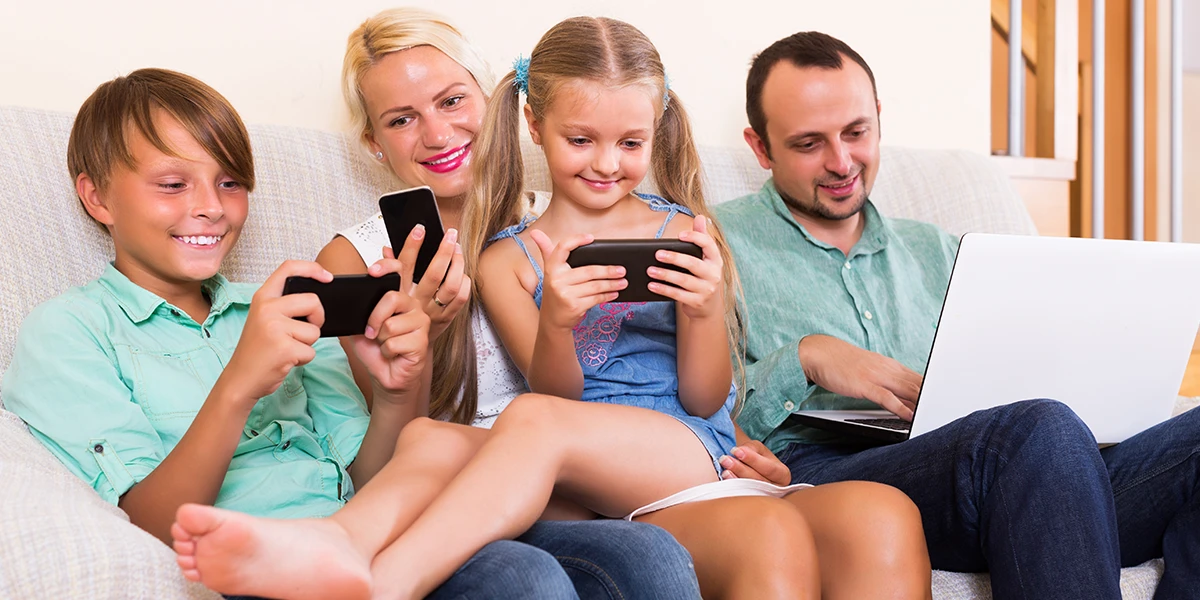 Eltern mit zwei Kindern, die Online-Spiele auf ihren Handys und Laptops spielen