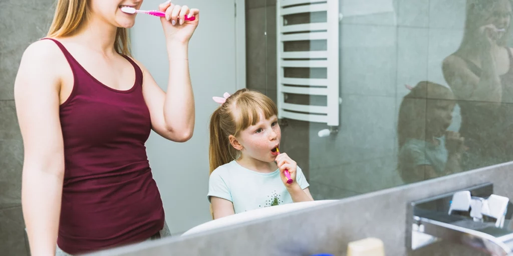 mother and daughter brushing their teeth in front of the bathroom mirror