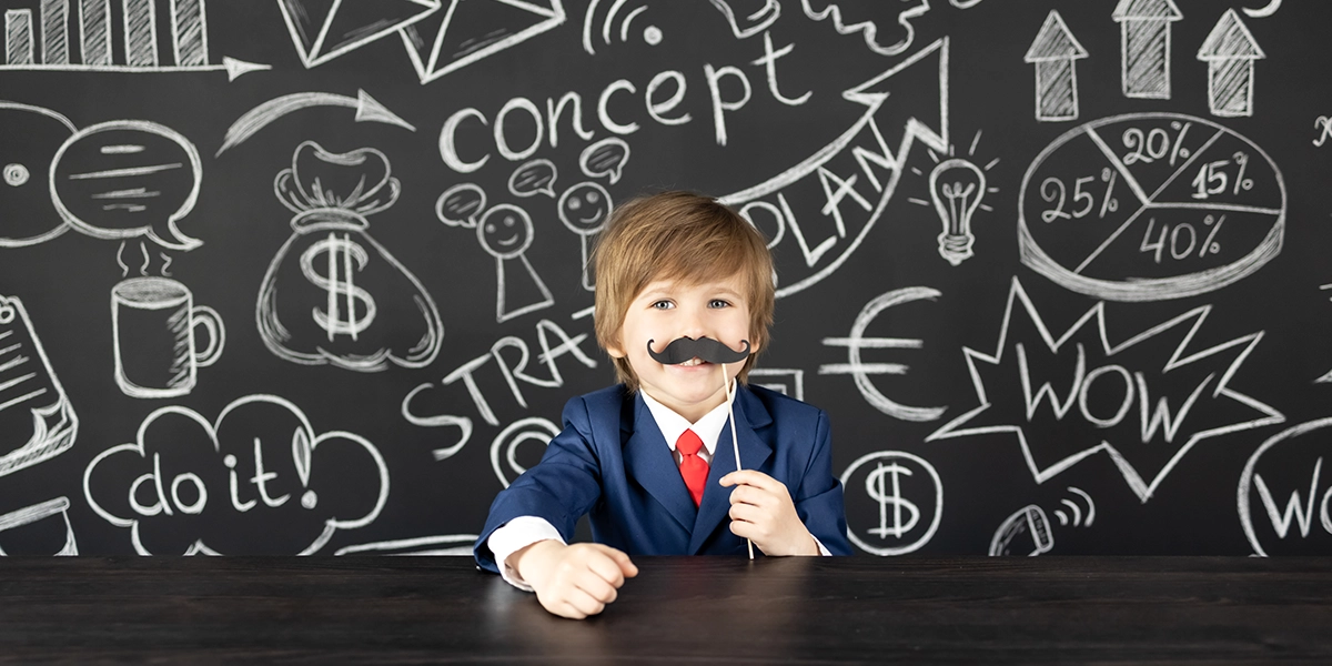 Boy in a suit wearing a mustache against a blackboard covered in career and business ideas