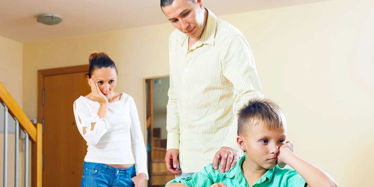 Concerned father and new partner looking at boy sitting at the table