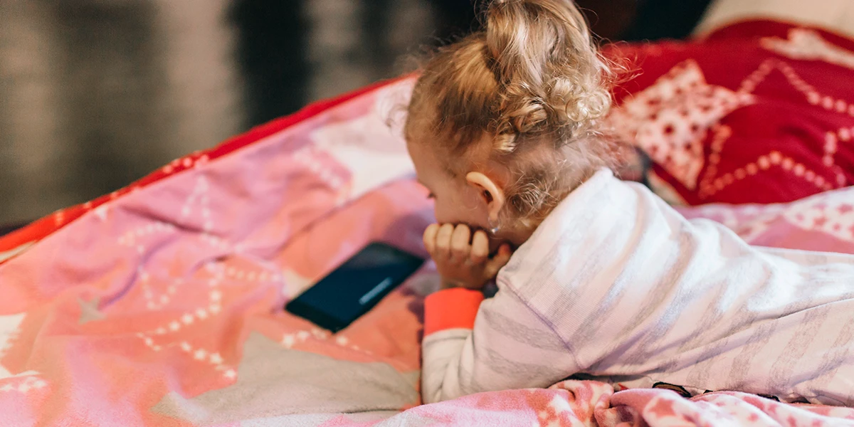 Kleinkind liegt in ihrem Bett und schaut auf ihr Handy