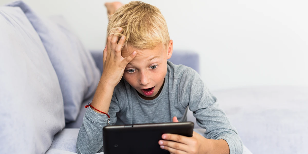 boy with shocked facial expression lying on the couch watching his tablet