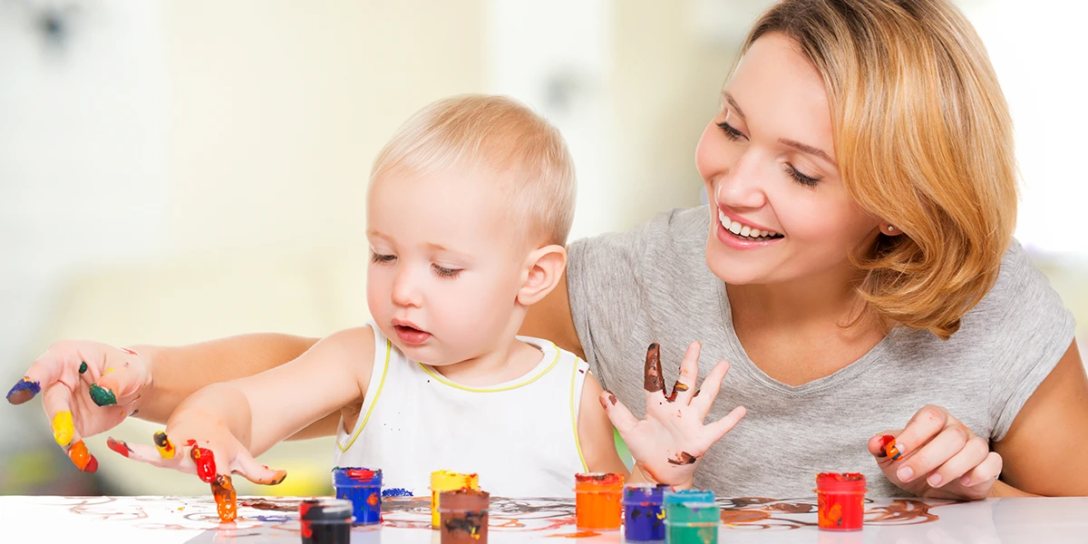Glückliche junge Mutter mit einem Kleinkind, das zu Hause mit den Händen malt
