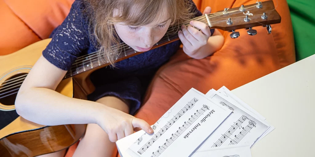 Mädchen liest Noten und übt Gitarre