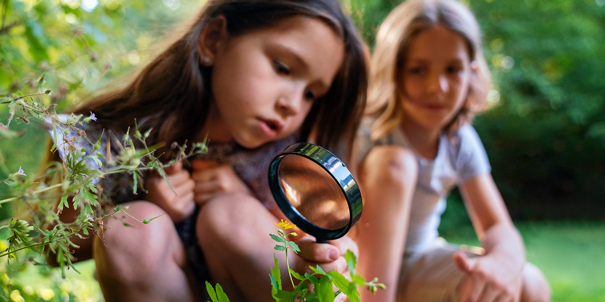 two girls in nature with one holding a magnifying glass