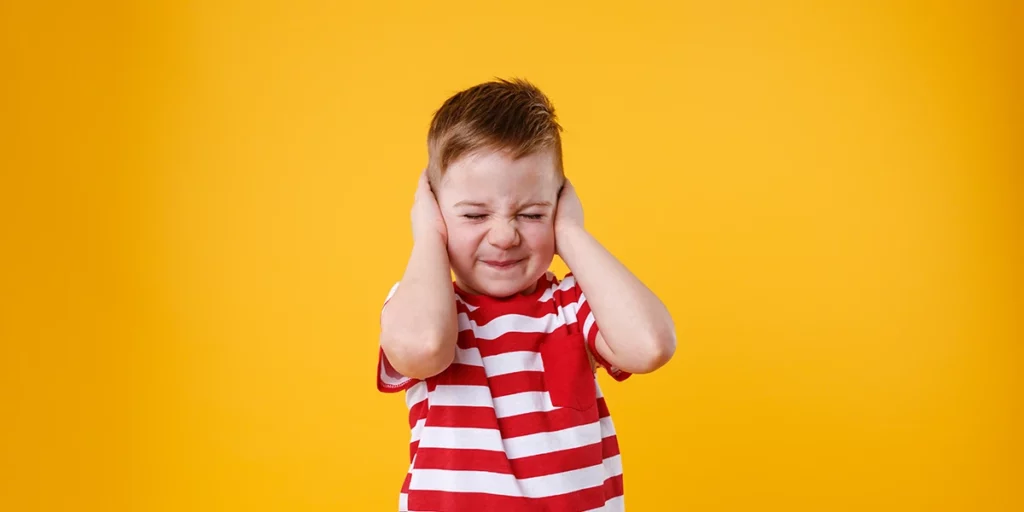 an angry unhappy irritated little boy covering ears and not listening to parents